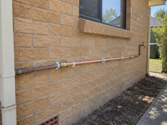 Repaired copper water pipe running along an exterior brick wall under a window in Whitebridge