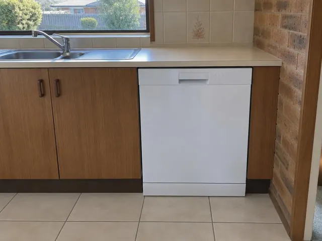 White dishwasher set under a kitchen benchtop beside wood cabinets and a tiled floor in Highfields