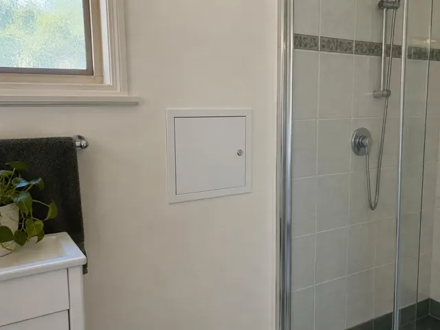 Bathroom wall with a small access panel beside a glass shower and towel rail in Dudley